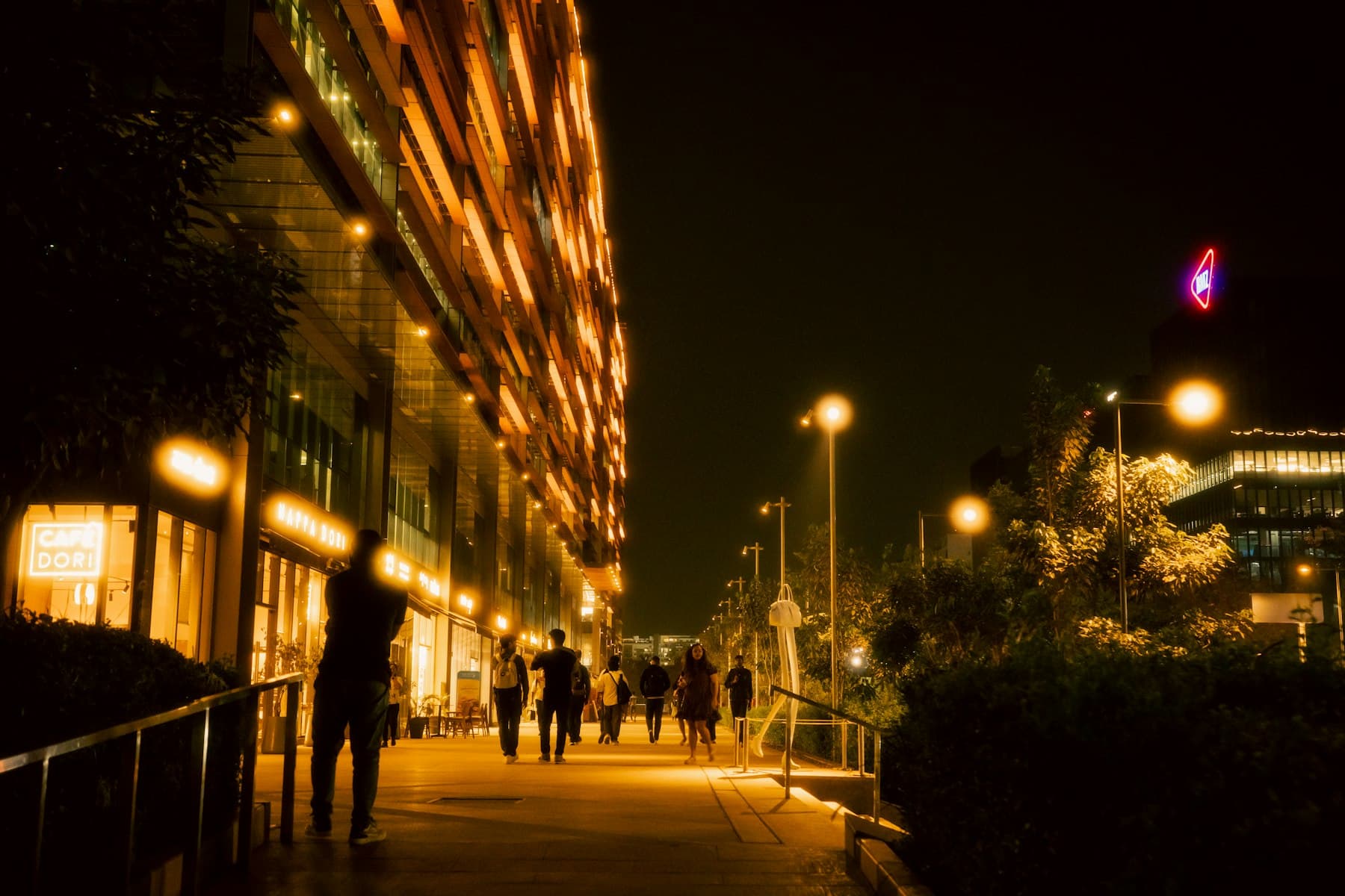 People walking through illuminated modern architecture in Bengaluru at night, representing the city's business districts and tech corridor energy.
