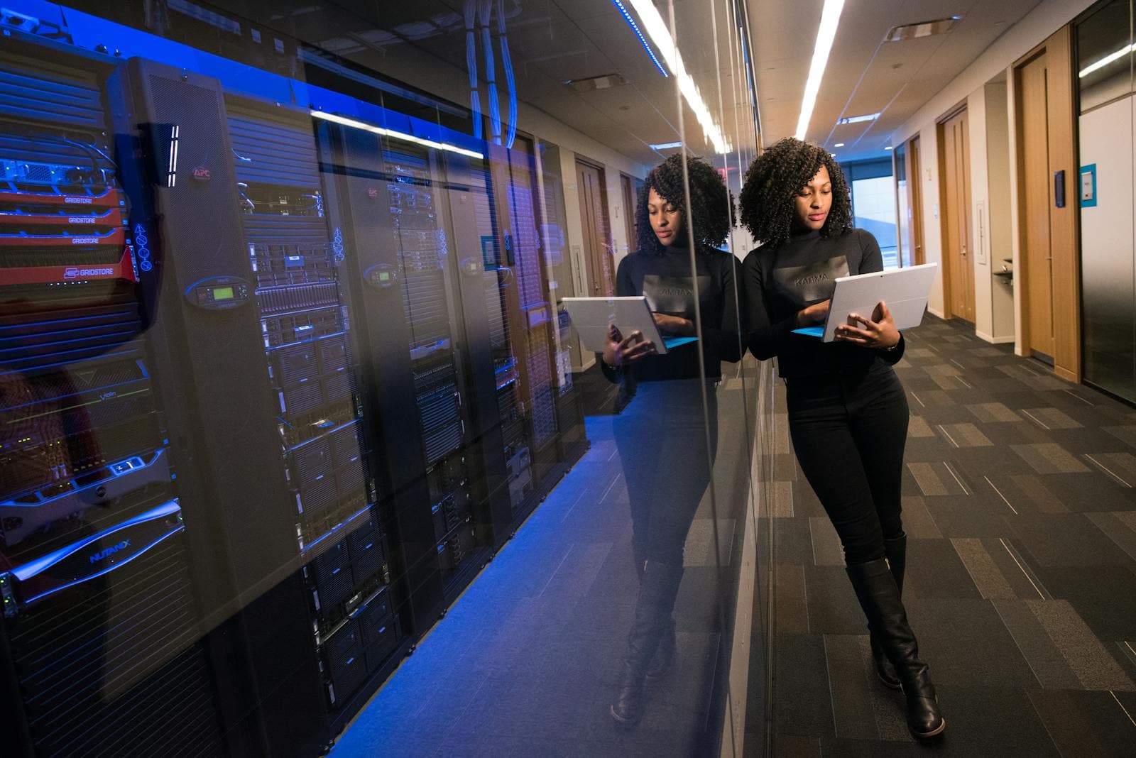 A woman engineer uses a laptop in a modern data center with server racks behind her