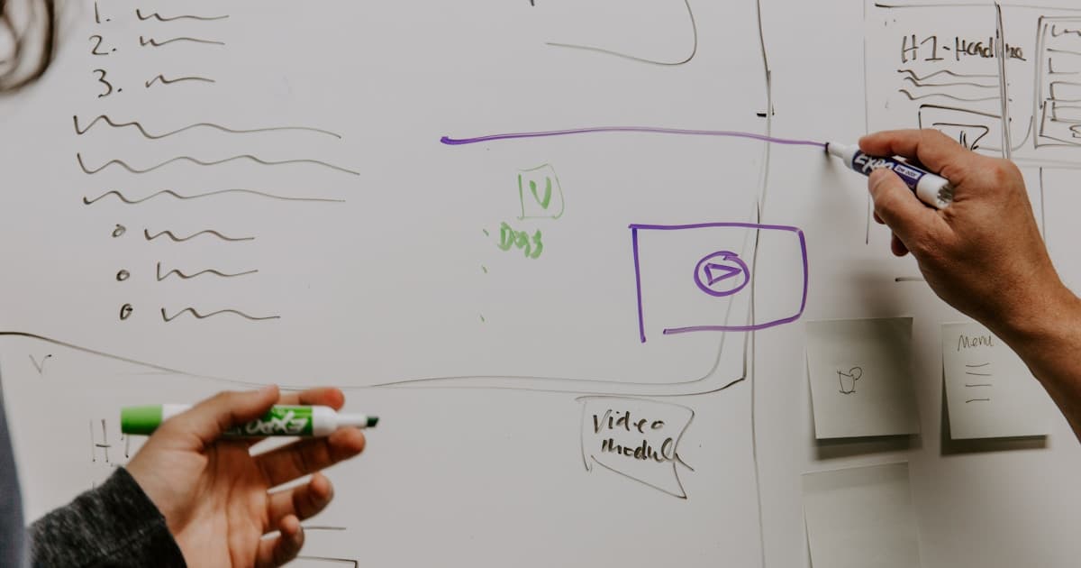 Two engineers collaborating at a whiteboard, sketching out a technical system design diagram together