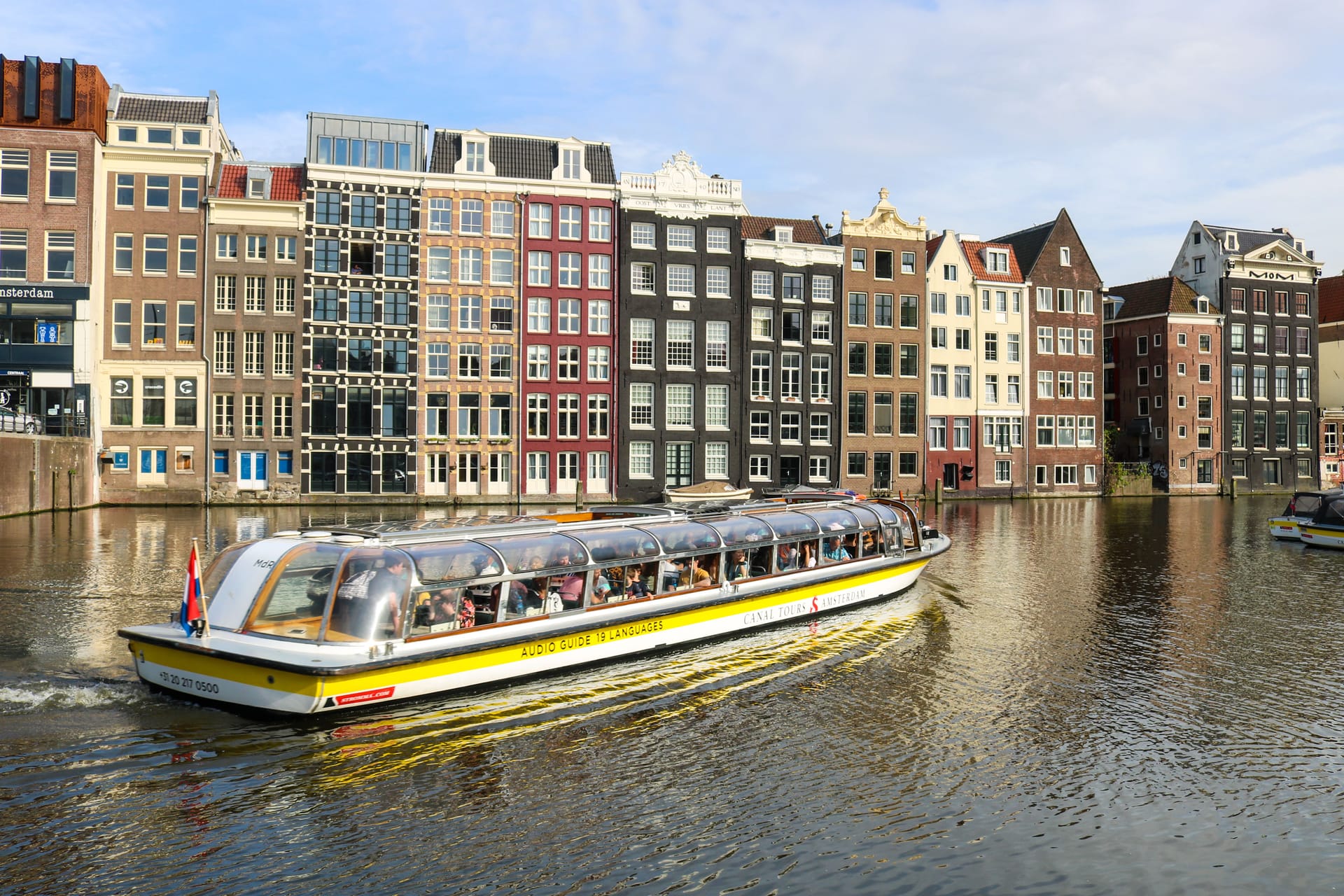 A canal boat moving through Amsterdam with historic houses along the water, representing the city's compact and connected work-life geography.