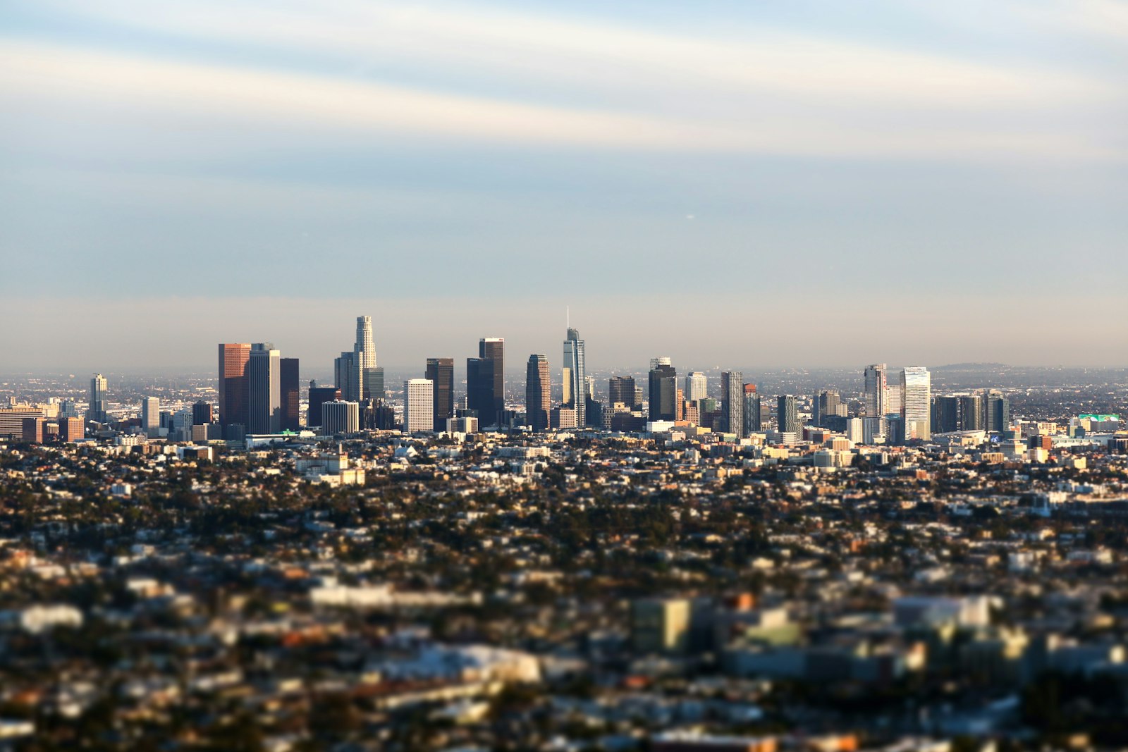 Downtown Los Angeles skyline under a cloudy sky with dense urban neighborhoods in the foreground