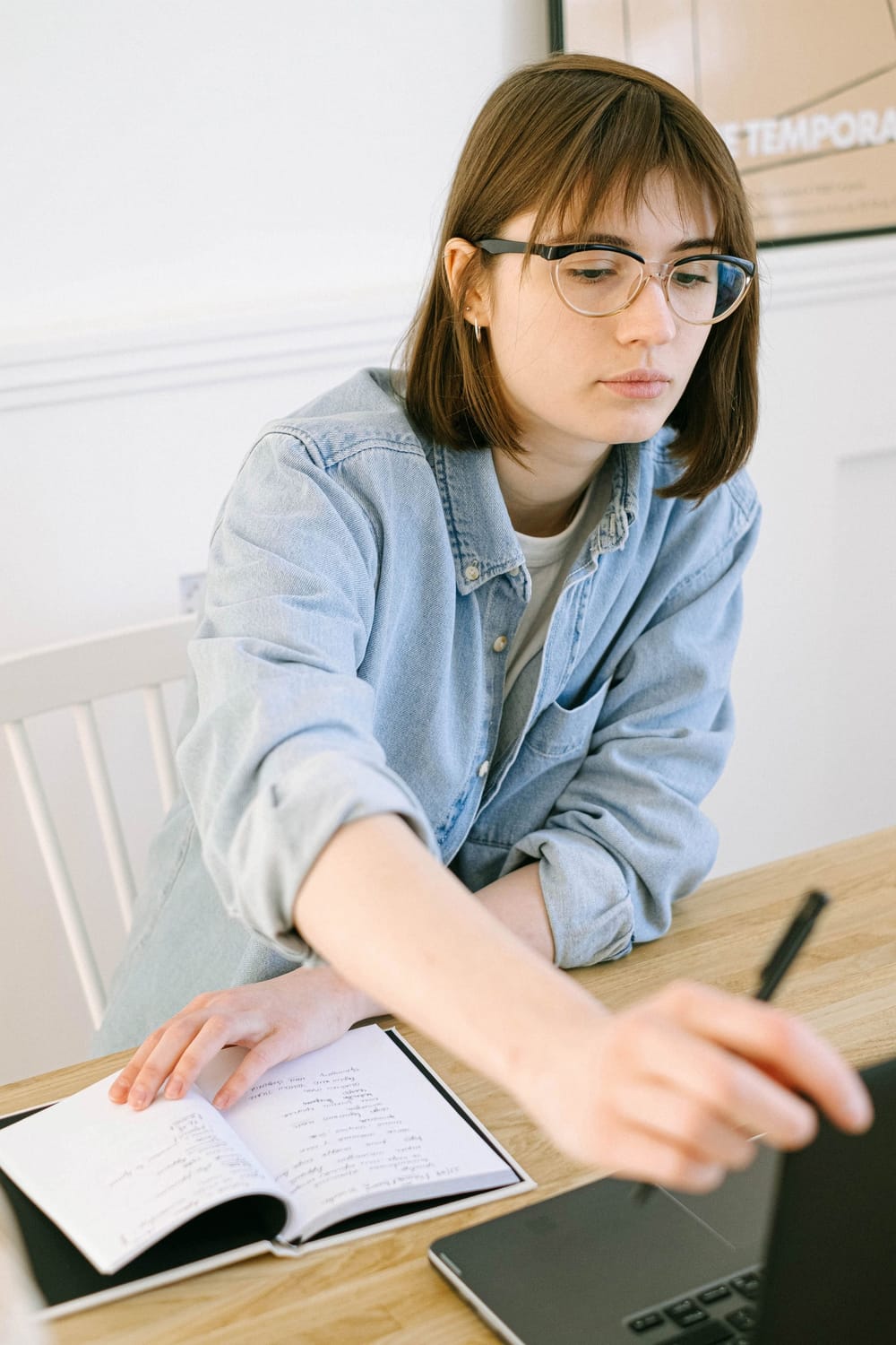 A woman reviewing her laptop while taking handwritten notes in a notebook.