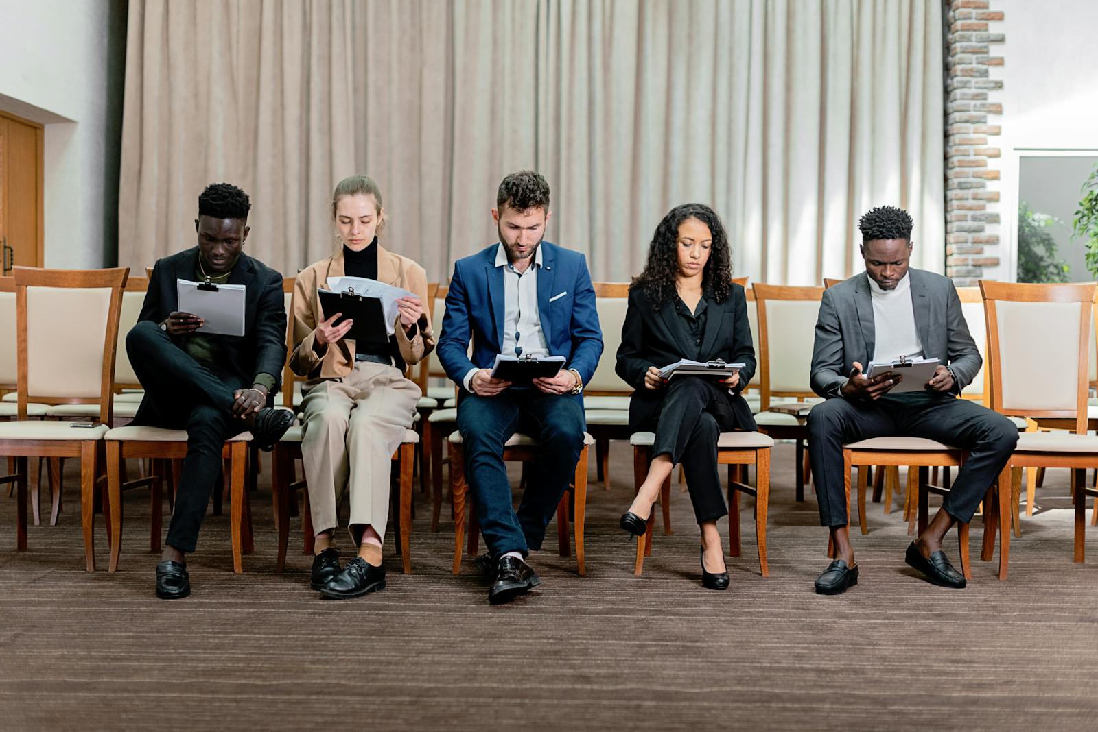A group of professionals sitting together with clipboards, representing the candidate pools, referrals, and human review process behind job board applications.