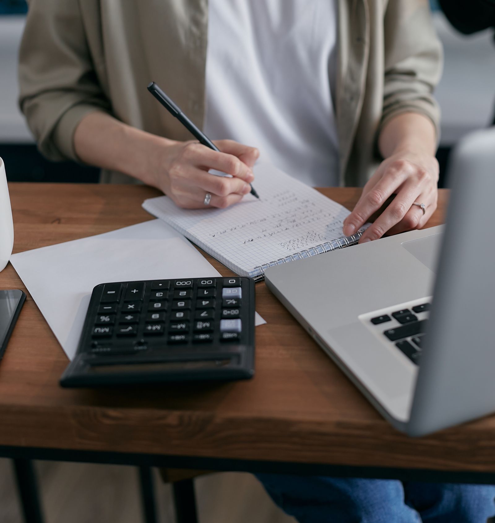 A person taking notes beside a calculator and laptop while researching market salary data for a role.