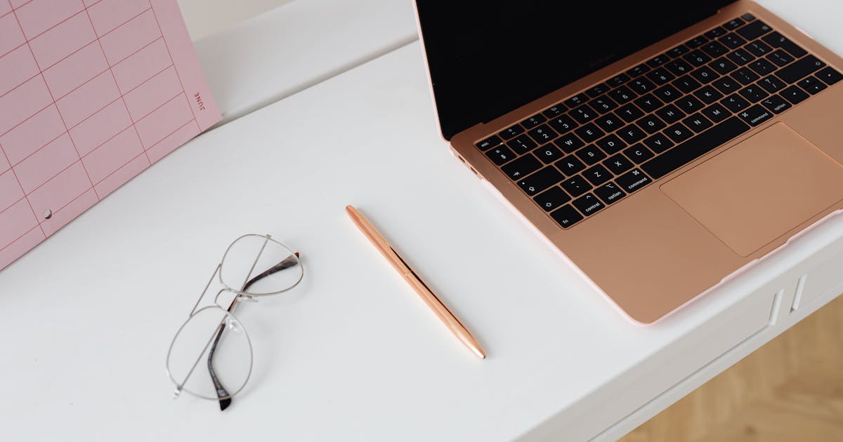 A clean and organized workspace with a laptop, planner, glasses, and pen on a desk, representing the final sign-off and review step before sending a thank-you email.